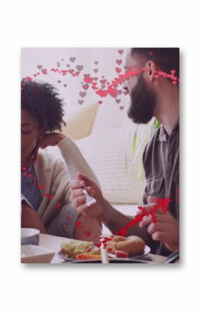 Image of hearts over happy diverse couple eating and talking