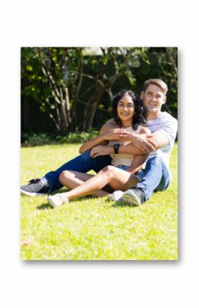 Sitting on grass, young couple hugging and smiling in sunny garden