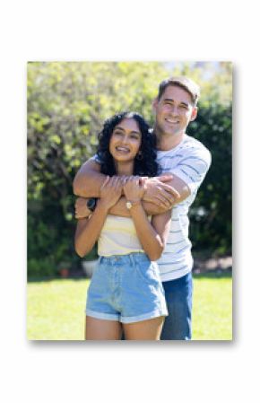 Smiling young couple embracing outdoors in sunny garden, enjoying time together