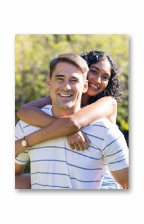 Smiling young couple enjoying piggyback ride outdoors in sunny park