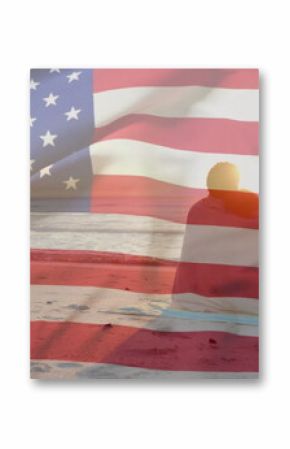 Image of american flag over happy diverse couple wrapped in rug embracing sat on sunset beach