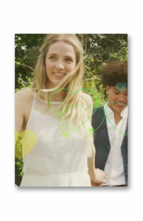 Image of colourful hearts over happy walking in garden on wedding day