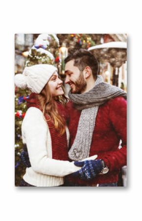 Young happy smiling couple posing on street. Models looking at each other, wearing stylish warm knitted sweaters, scarves, gloves, hat