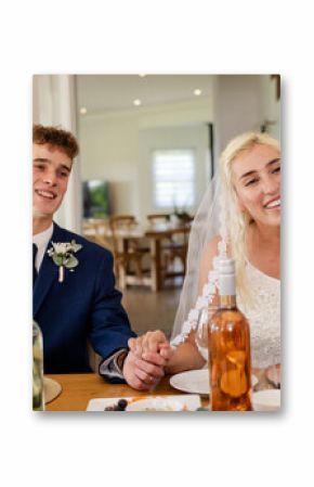 Bride and groom smiling, holding hands at wedding reception table indoors