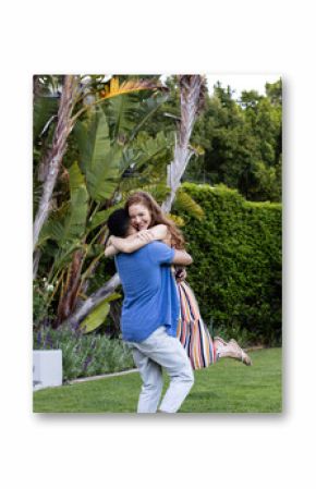 Young couple embracing joyfully in lush garden, surrounded by vibrant greenery