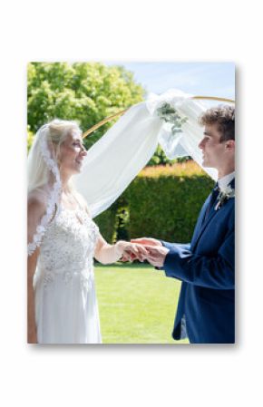 Bride and groom exchanging vows outdoors under elegant floral arch, smiling warmly