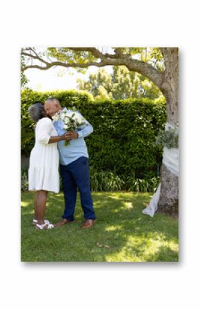 Senior couple embracing under tree, holding bouquet, celebrating love outdoors
