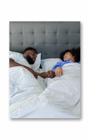 Couple relaxing in bed, holding hands and smiling, enjoying peaceful morning