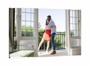 Couple embracing on balcony, enjoying sunny day with lush greenery view