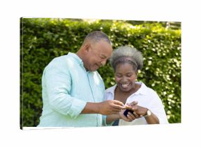 Exchanging rings and smiling, African American senior couple celebrating love in garden
