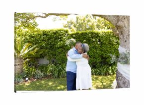 Senior couple embracing under tree in garden, enjoying peaceful moment together