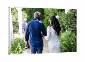 Bride and groom walking arm in arm through lush garden, smiling joyfully