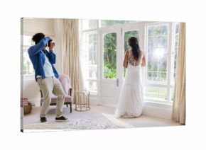 Photographer capturing bride in elegant gown standing by large window