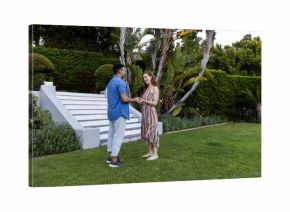 Young couple holding hands and smiling in lush garden setting