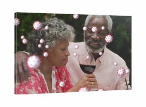 Holding wine glasses senior couple hugging in pink attire at garden table, with virus graphics