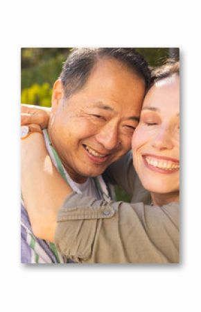 Smiling multiracial middle-aged couple embracing outdoors, enjoying time together in sunlight