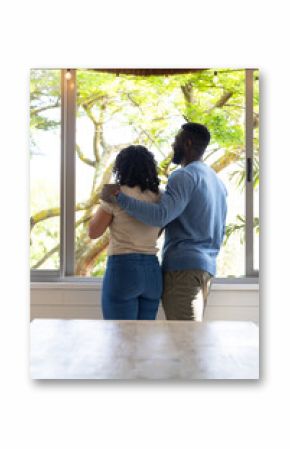 multiracial couple embracing by window, enjoying peaceful view of nature together, at home