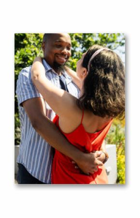 Diverse couple embracing smiling and enjoying sunny day in garden
