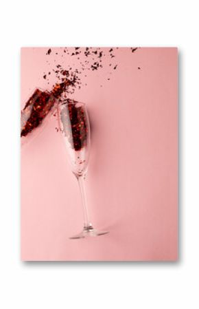 Two champagne glasses spilling red glitter confetti on pale pink background with copy space