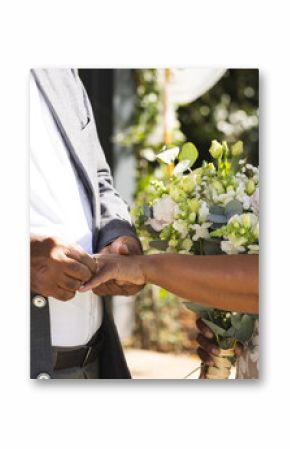 Midsection of senior biracial groom putting wedding ring on finger of bride