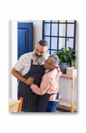 Wearing aprons, senior couple dancing together in cozy kitchen