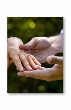 Showing engagement ring, groom holding bride's hand at outdoor wedding