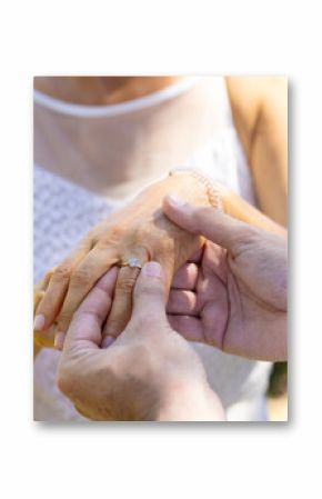 Placing engagement ring on bride's finger, bride and groom at outdoor wedding