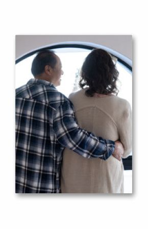 Senior couple hugging while looking out round window on vacation