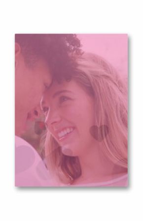 Image of hearts and pink tint over happy diverse couple embracing at outdoor wedding