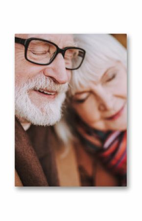 Close up portrait of senior gentleman in glasses cuddling with his lady and smiling. Focus on male pensioner