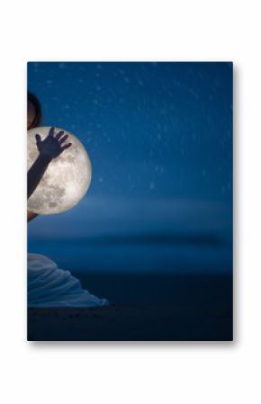 Tender image of a girl  female magic. Beautiful attractive girl on a night beach with sand and stars hugs the moon, art photo. On a dark background with space.