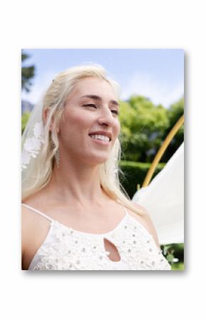 Bride smiling joyfully during outdoor wedding ceremony, surrounded by lush greenery