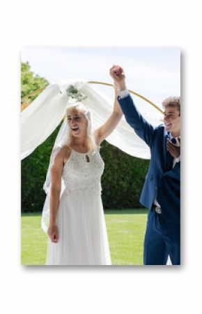 Bride and groom celebrating under arch while guests applaud in garden ceremony
