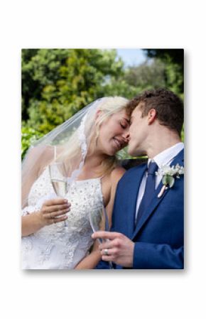 Bride and groom sharing romantic moment on garden bench, holding champagne glasses
