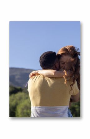 Young couple embracing outdoors with mountains in background, sharing joyful moment