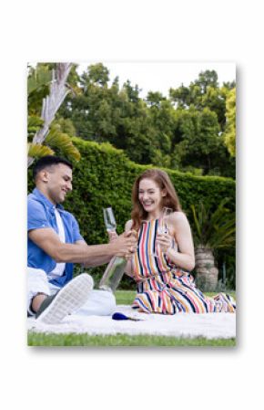 Young couple enjoying picnic outdoors, sharing champagne and smiling on blanket