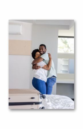 African American Couple embracing joyfully in bedroom with suitcase on bed, celebrating reunion