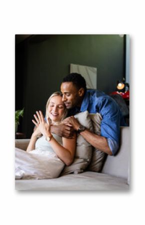Couple celebrating engagement at home, smiling and embracing on cozy sofa