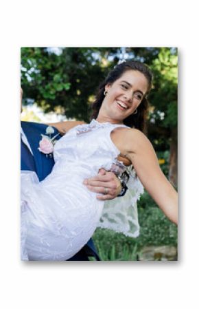 Groom joyfully carrying bride in garden, both smiling and celebrating their wedding
