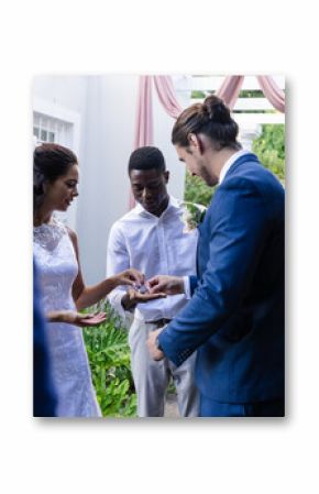 Bride and groom exchanging rings outdoors, surrounded by friends and family