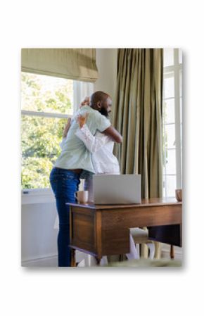 Couple embracing warmly at home, laptop and coffee mugs on wooden desk