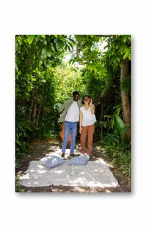 Couple enjoying romantic outdoor picnic under lush green trees, smiling and relaxed