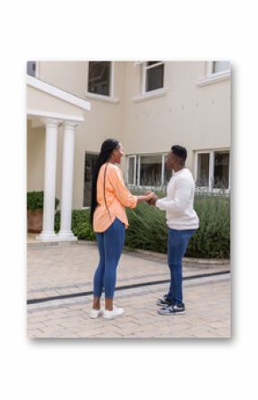 African American couple standing outside home, holding hands and smiling warmly