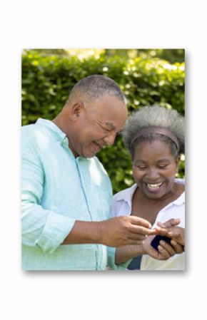 Exchanging rings and smiling, African American senior couple celebrating love in garden