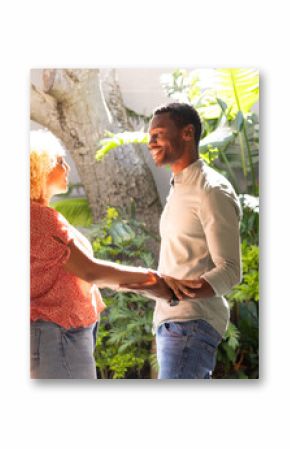 Couple holding hands and smiling, enjoying sunny day in lush garden