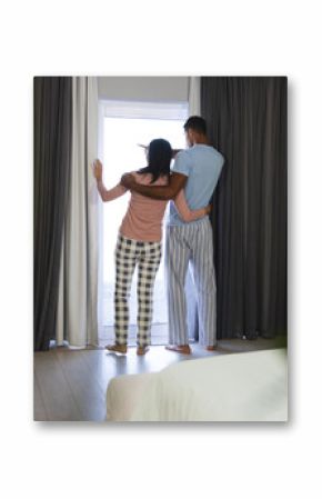 Couple in pajamas standing by window, embracing and enjoying morning view