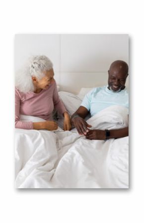 Smiling senior African American couple reaching toward each other's hands on bed, with lamp