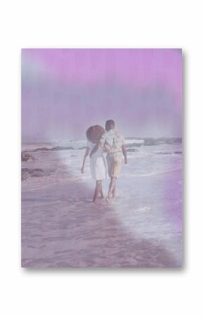 Walking couple wearing summer clothes holding arms along beach, with gentle surf and rocky outcrops