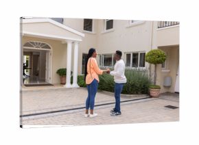 African American couple standing outside home, holding hands and smiling warmly