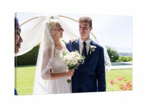 Bride and groom smiling joyfully outdoors, holding bouquet in sunny garden
